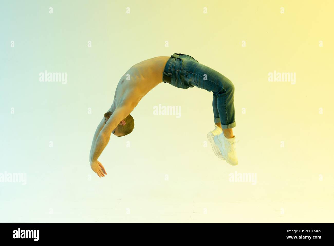 Adatta l'atleta maschile che esegue un salto flick flick o indietro handspring in una vista laterale a tutta lunghezza su uno sfondo colorato studio Foto Stock