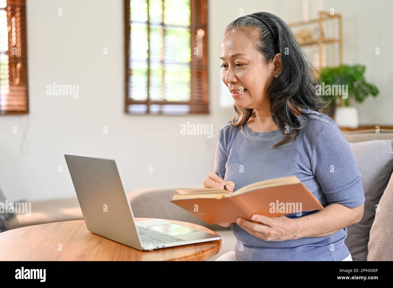 Bella e felice Asia-età pensionato donna sta imparando una lezione online a casa, alla ricerca di ricette alimentari su Internet e scherzo nel suo libro, Foto Stock