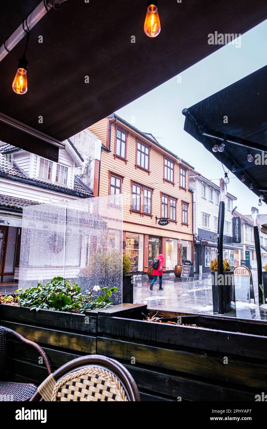 Snandnes, Norvegia, 13 2023 marzo, Donna indossa Un cappotto rosso camminando lungo il centro di Sandnes High Street in The Rain Passing Shop fronts with No Other Peo Foto Stock