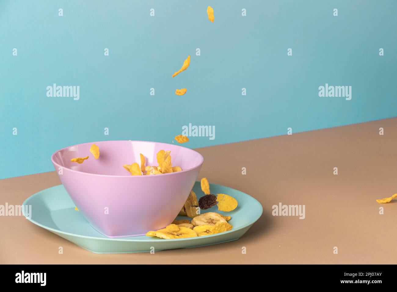 Colazione sana in ciotola rosa, banana chips, cornflakes, sfondo blu, sala copia Foto Stock