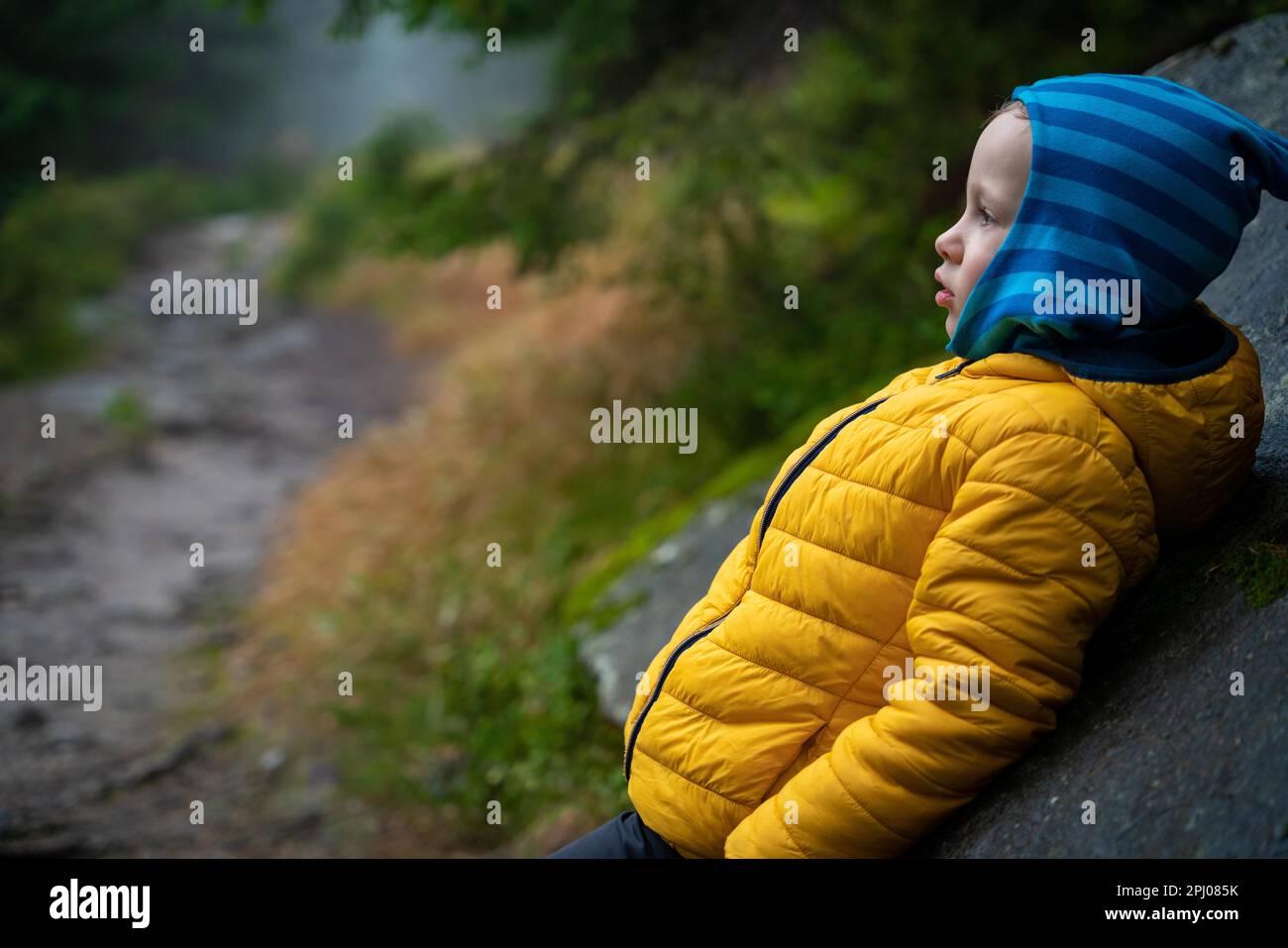 Il bambino riposa sul sentiero di montagna, in piedi appoggiato contro un grande masso. Montagne polacche Foto Stock