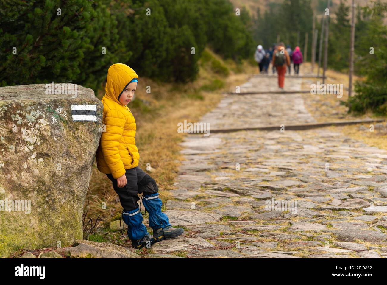 Il bambino riposa sul sentiero di montagna, in piedi appoggiato contro un grande masso. I turisti stanno marciando sullo sfondo. Montagne polacche Foto Stock