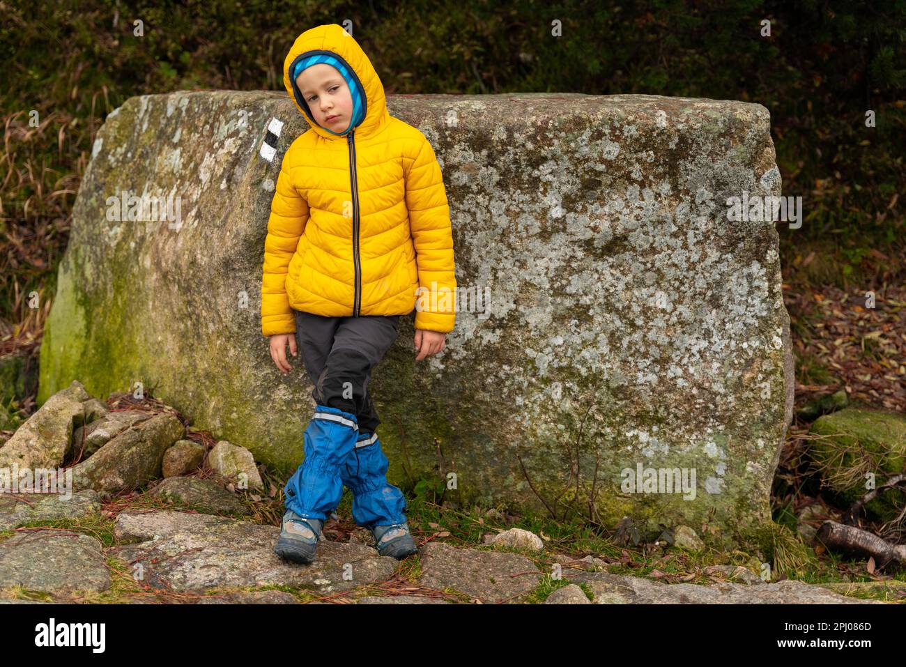 Il bambino riposa sul sentiero di montagna, in piedi appoggiato contro un grande masso. Montagne polacche Foto Stock