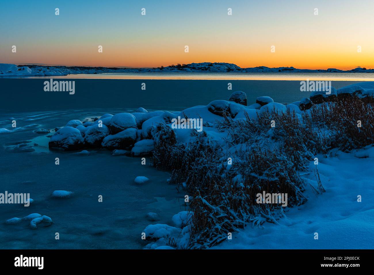 Uno splendido tramonto invernale illumina il tranquillo mare ghiacciato e la terra innevata della Svezia, mostrando la bellezza della natura. Foto Stock