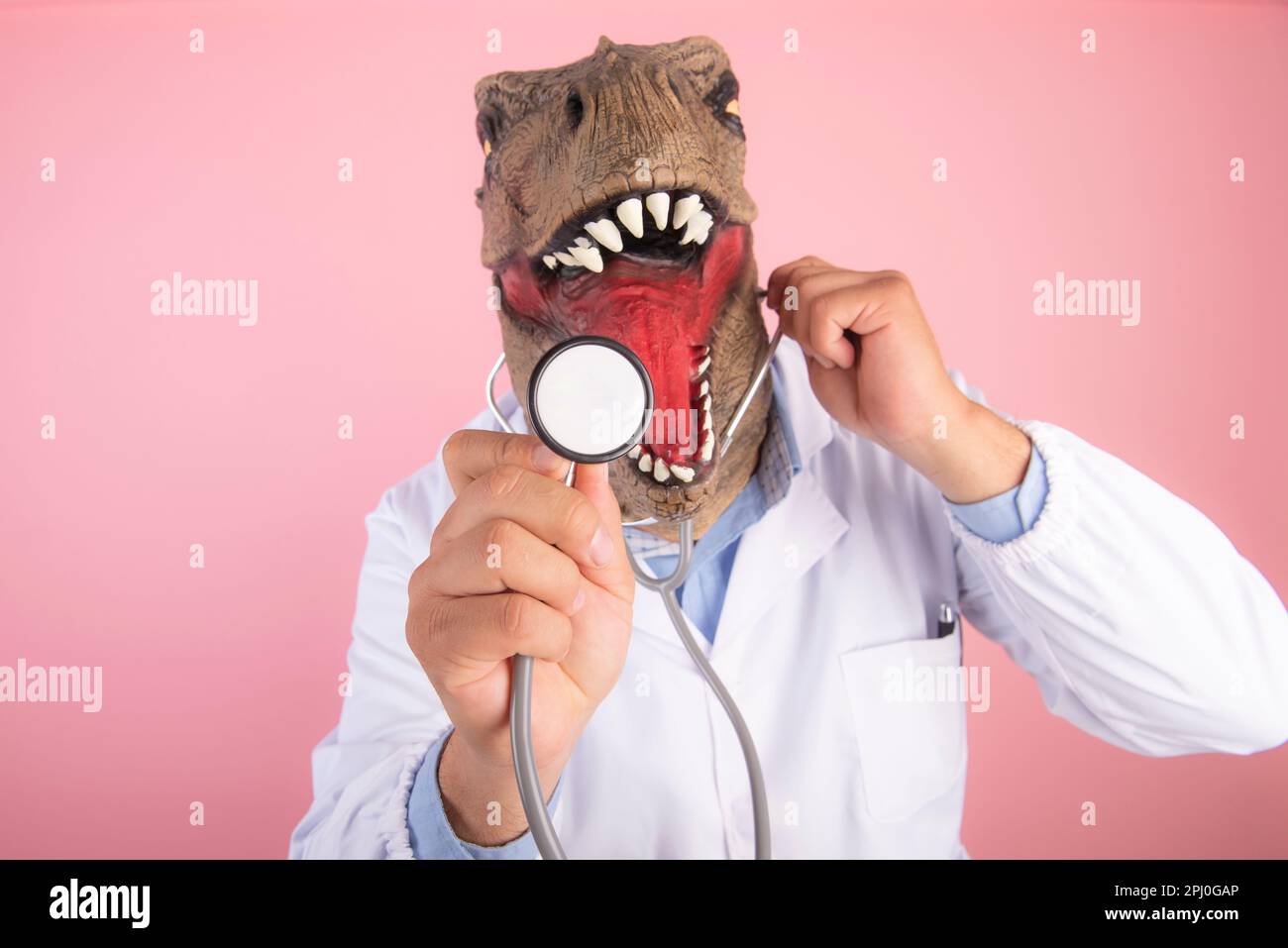 Medico con maschera T Rex che tiene uno stetoscopio in primo piano su uno sfondo rosa isolato. messa a fuoco selettiva Foto Stock