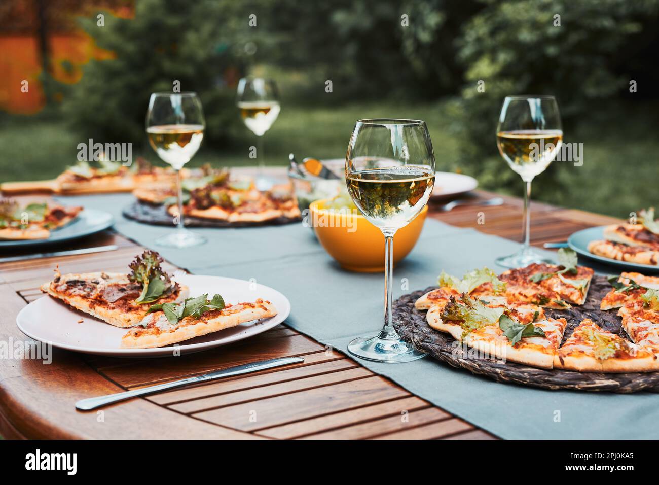 Cena in un giardino di casa. Pizza, insalate, frutta e vino bianco su tavola in un frutteto in un cortile Foto Stock