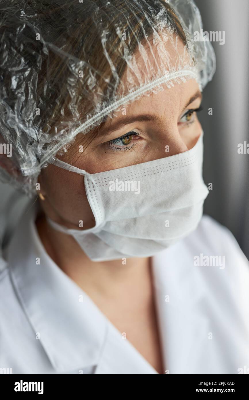 Medico con il viso coperto di maschera. Ritratto di giovane donna che indossa l'uniforme, cappuccio e maschera per evitare l'infezione da virus e per prevenire la diffusione di di Foto Stock