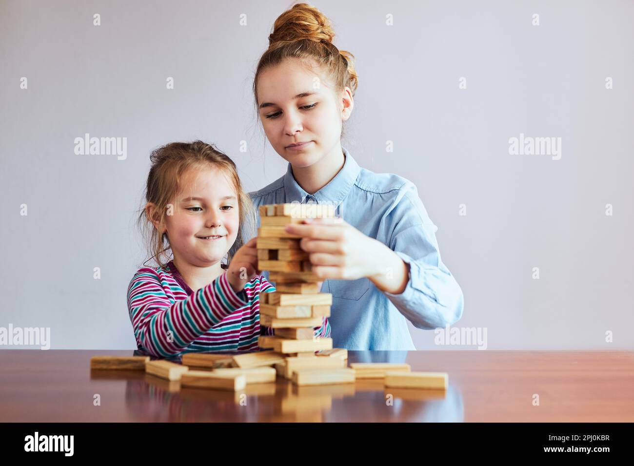 Bambina preschooler e sua sorella maggiore giocando insieme con il gioco blocchi di legno giocattolo. Fratelli che trascorrono del tempo seduti alla scrivania a casa Foto Stock