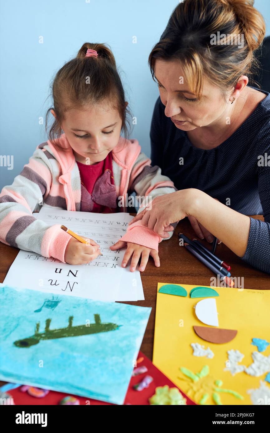 Bambina preschooler imparare a scrivere lettere con l'aiuto di sua madre. Capretto che scrive le lettere, disegni le immagini, fare il roba con la carta, fare un hom Foto Stock