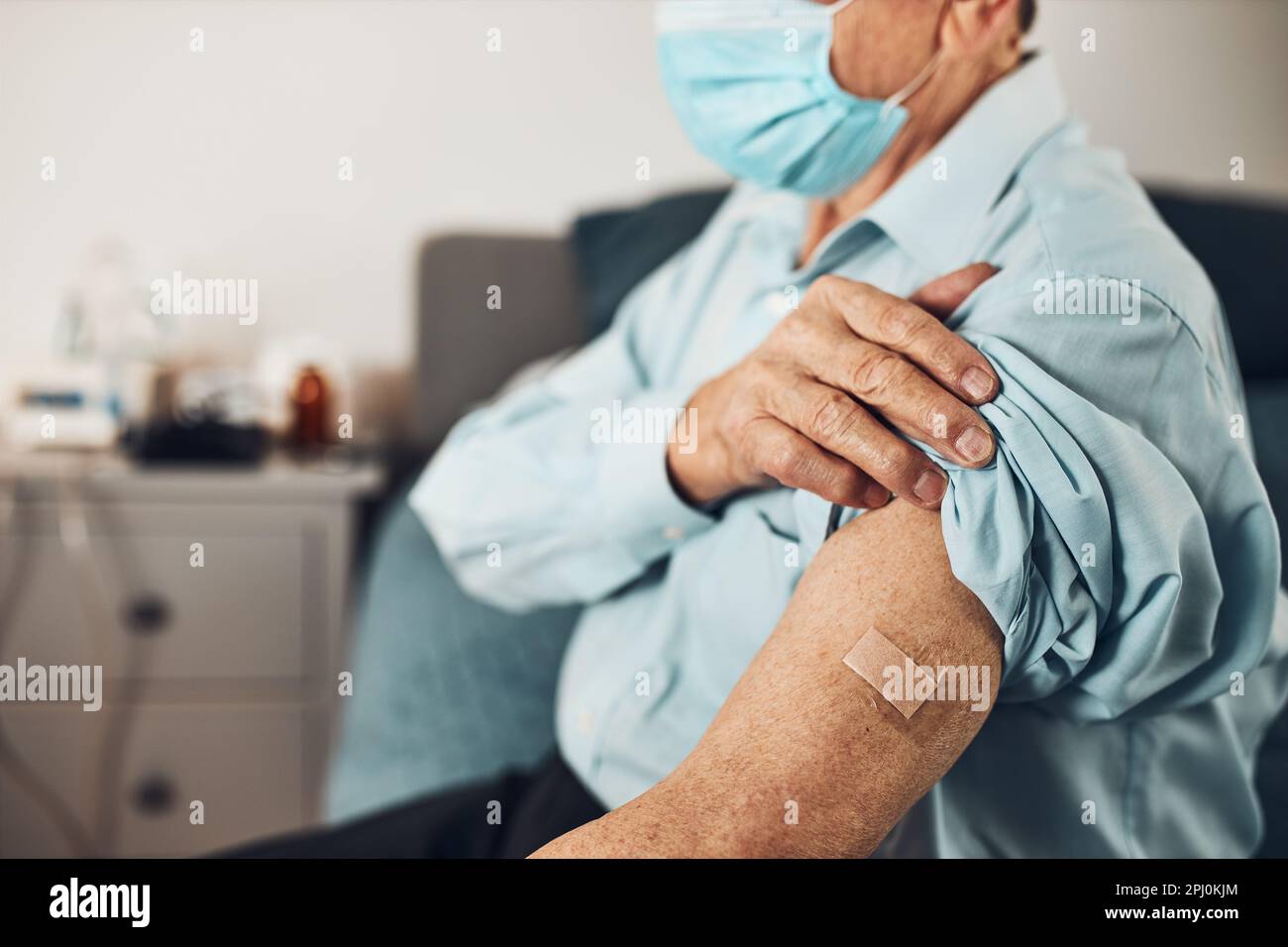 Paziente anziano che tiene la camicia manica in su con un gesso al posto dell'iniezione del vaccino. Covid-19 o vaccinazione contro coronavirus. Uomo che indossa maschera facciale Foto Stock