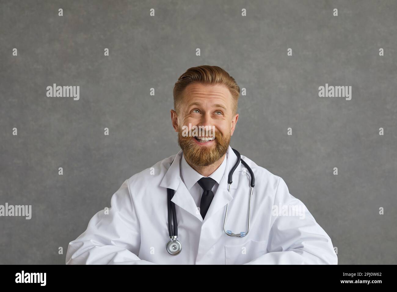 Ritratto di felice medico maschio guardando via, pensando a qualcosa, sorridendo e ridendo Foto Stock