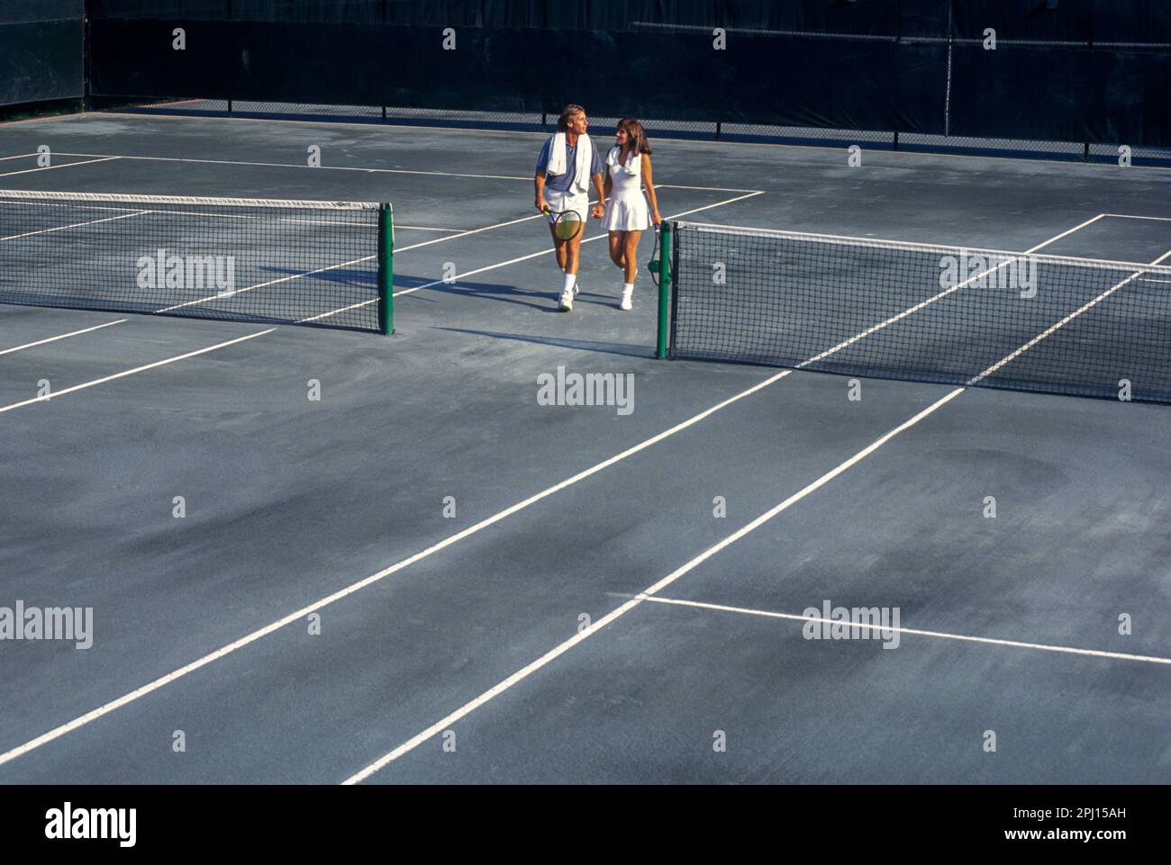 GIOVANE COPPIA CHE CAMMINA INSIEME SUL CAMPO DA TENNIS IN TERRA BATTUTA Foto Stock