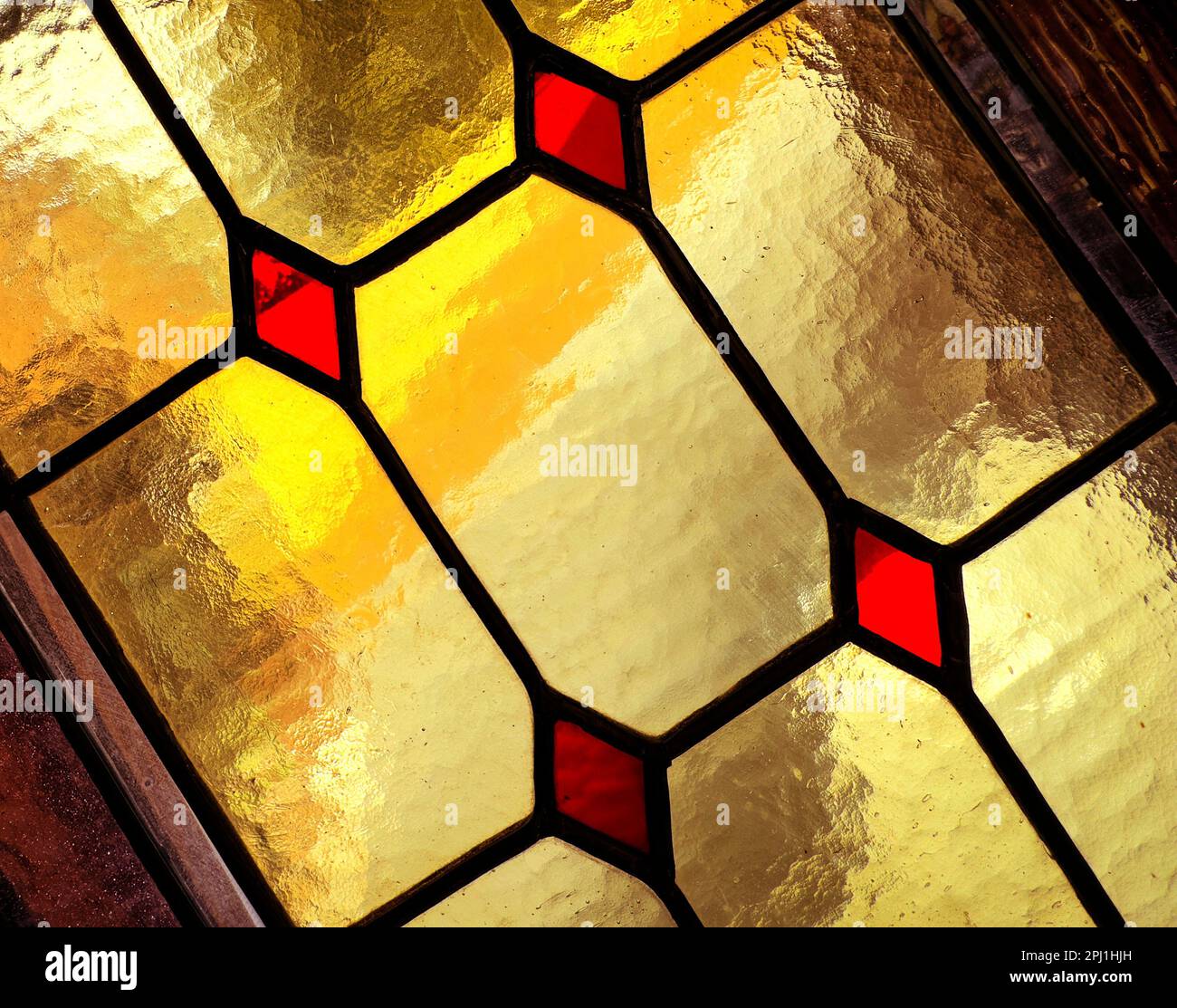 Il primo piano mostra una finestra di vetro colorato sulla diagonale con pannelli rettangolari e diamantati in giallo e rosso. Contorni in piombo nero e cornice in legno visibili. Foto Stock