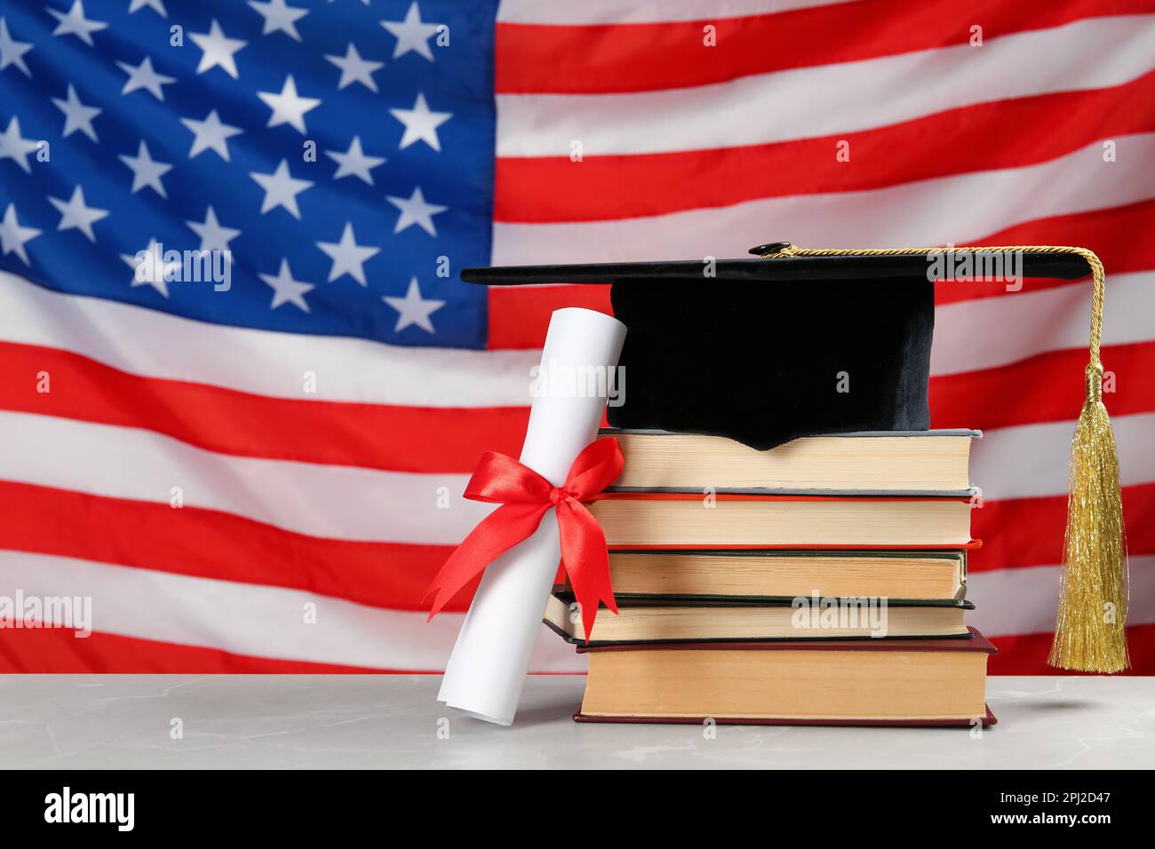 Cappello di laurea, libri e diploma su tavolo grigio chiaro contro la bandiera degli Stati Uniti. Spazio per il testo Foto Stock
