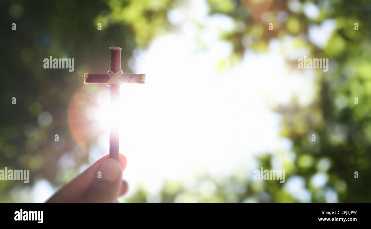 Fresco cielo blu del mattino e verde lussureggiante foresta di alberi sfondo e luminoso sole che splende attraverso la croce di Gesù Cristo in mano Foto Stock