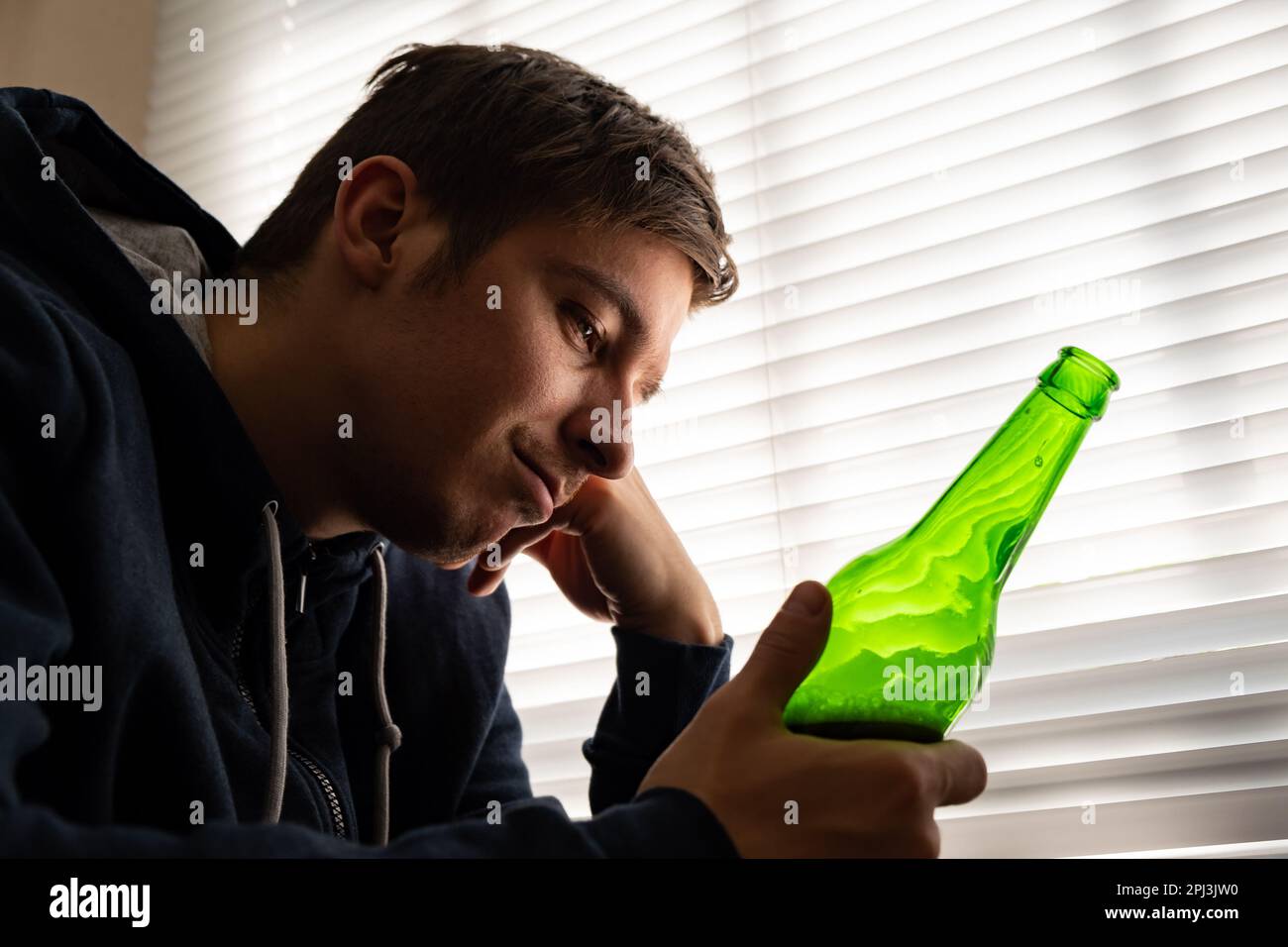 Giovane uomo con una birra alla finestra nella stanza Foto Stock