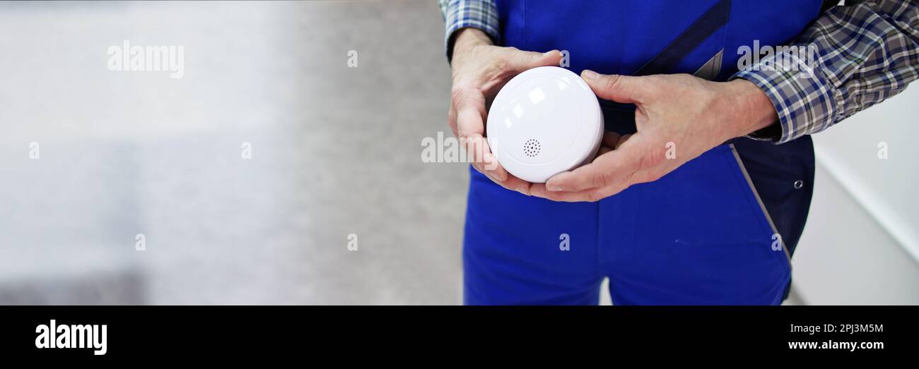 Elettricista che tiene rivelatore di fumo. Test e installazione dell'allarme antincendio Foto Stock