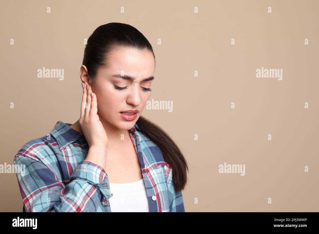 Giovane donna che soffre di dolore all'orecchio su sfondo beige. Spazio per il testo Foto Stock