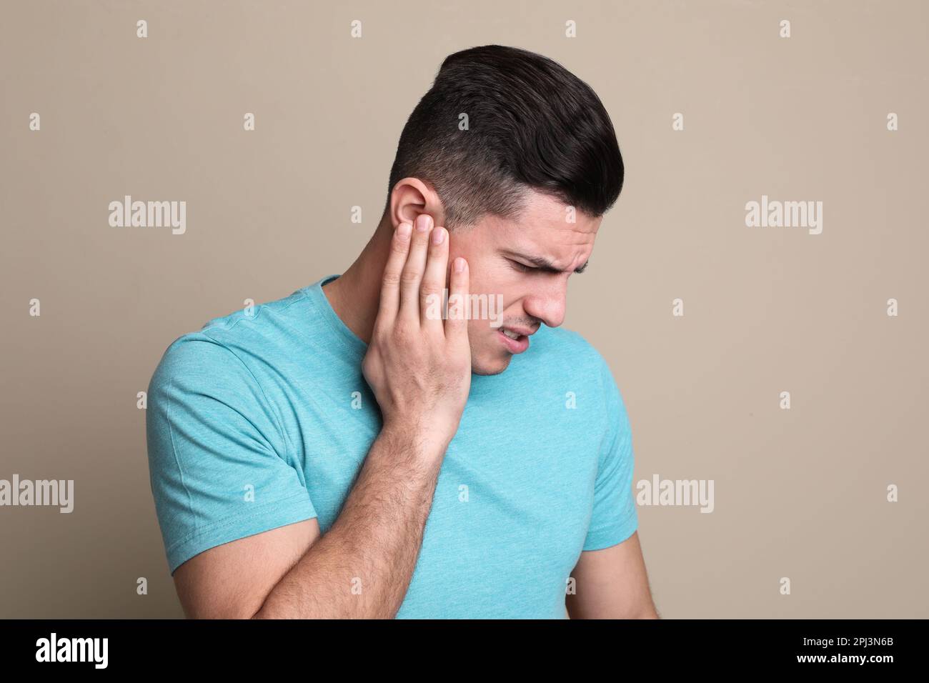 Uomo che soffre di dolore all'orecchio su sfondo beige Foto Stock