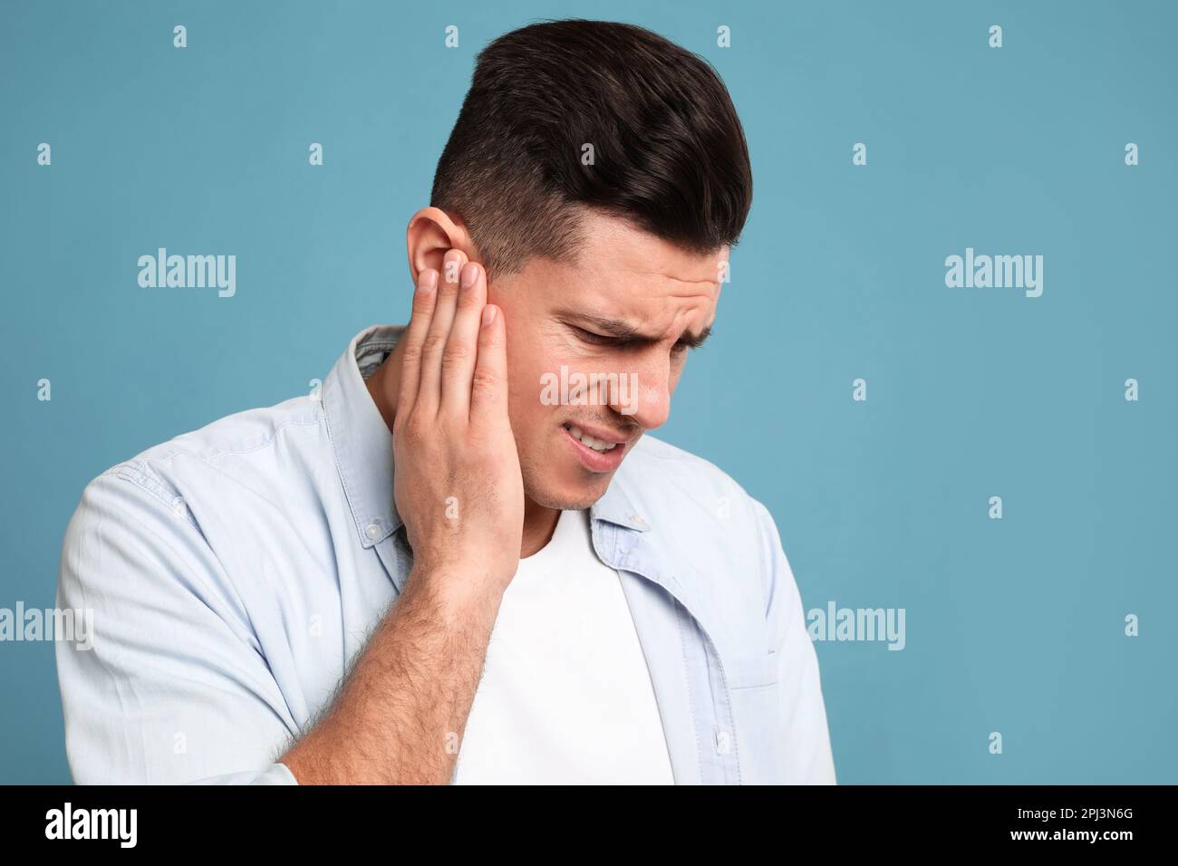 Uomo che soffre di dolore all'orecchio su sfondo azzurro. Spazio per il testo Foto Stock