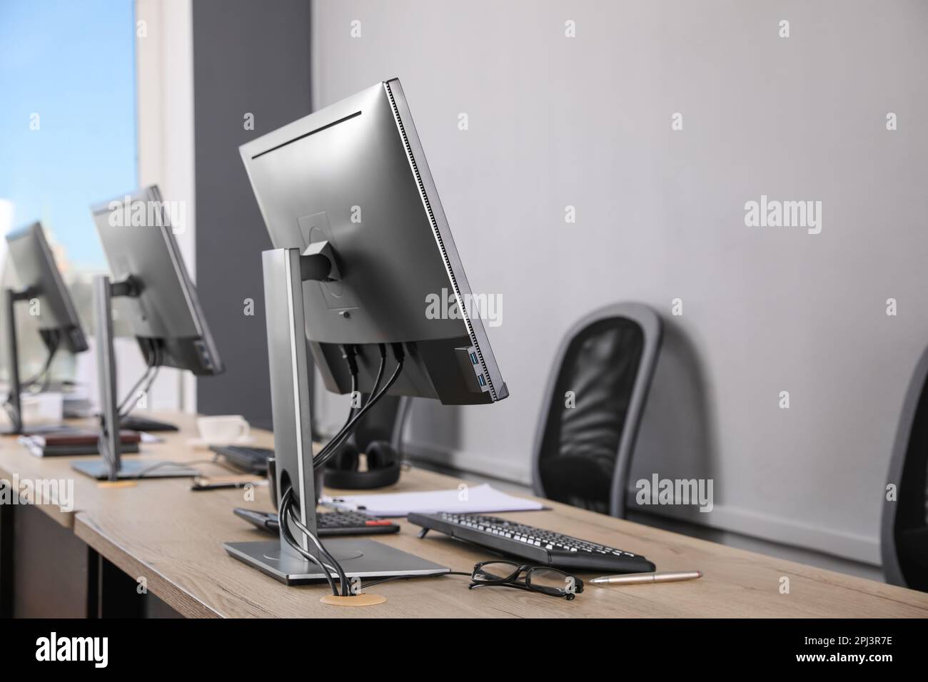 Interno ufficio aperto. Posti di lavoro moderni con computer vicino a una parete grigio chiaro Foto Stock