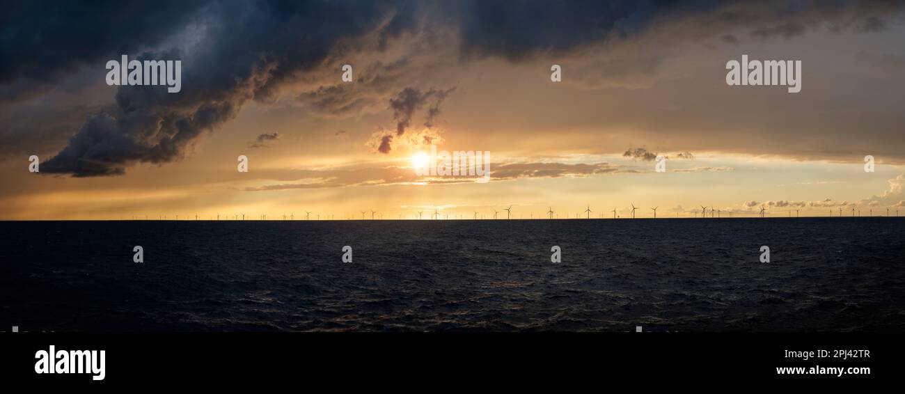 Una tempesta che arriva nel Mare del Nord al largo della costa inglese al tramonto con una fattoria a vento all'orizzonte. cielo spettacolare, nuvole e luce sull'oceano. Foto Stock