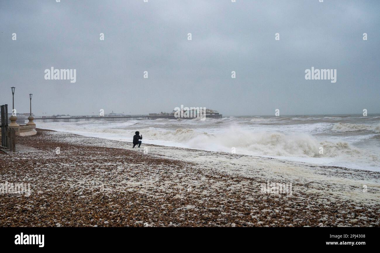 Brighton UK 31st marzo 2023 - Un camminatore si ferma per scattare foto sulla spiaggia di Brighton all'inizio di questa mattina come Storm Mathis batte la costa meridionale oggi con venti previsti per raggiungere 70mph in alcune aree: Credit Simon Dack / Alamy Live News Foto Stock