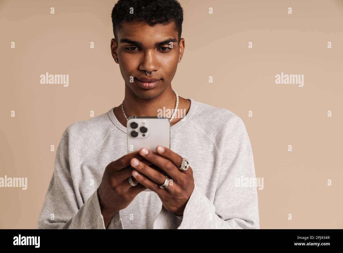 Giovane uomo nero con posa piercing e utilizzando il telefono cellulare  isolato su sfondo beige Foto stock - Alamy