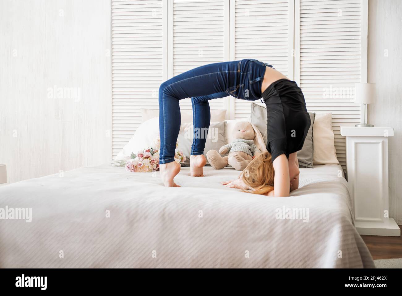 ragazza giovane che fa ginnastica su sfondo bianco, la ragazza fa un ponte di ginnastica, sul letto, nella stanza Foto Stock