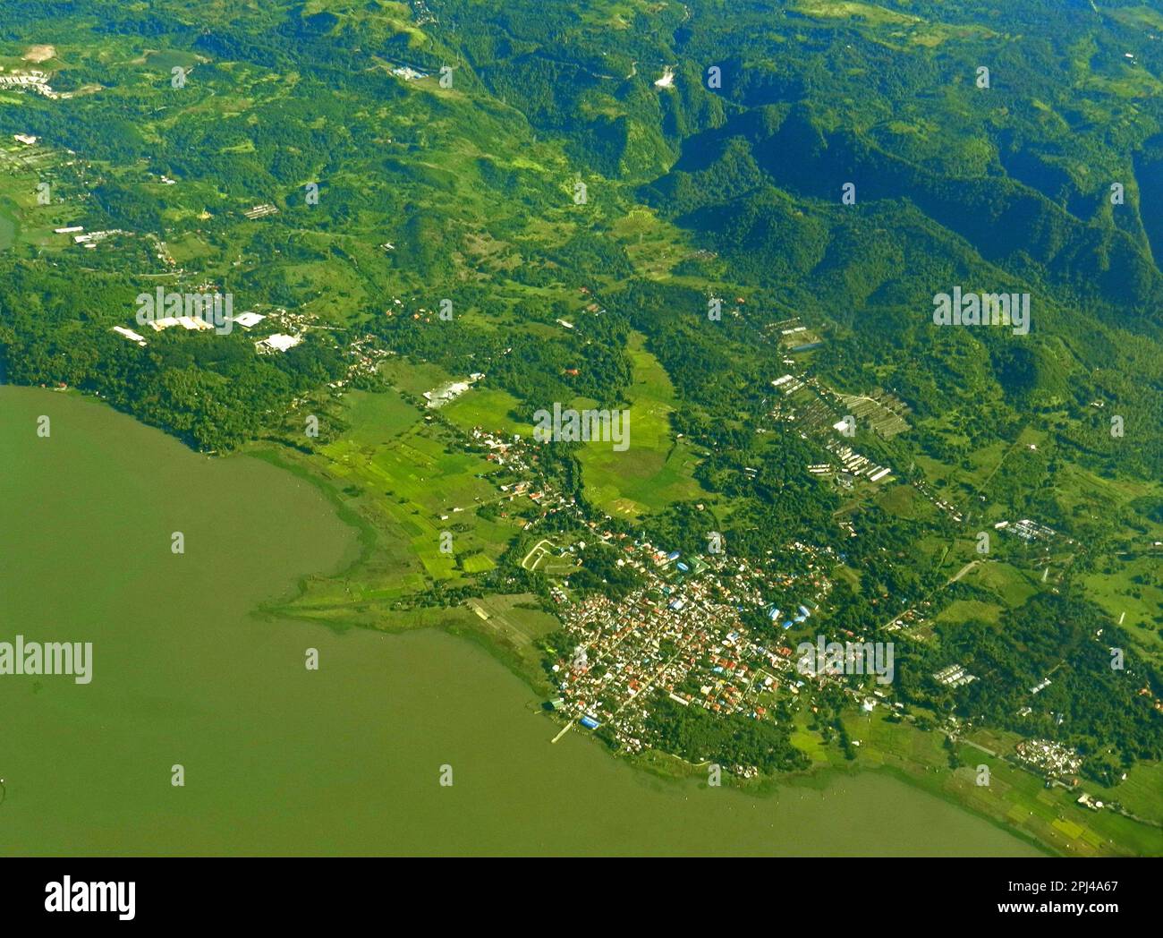 Arcipelago filippino: Vista aerea di una città costiera con molo di sbarco, sostenuto da gamme di colline boscose. Foto Stock