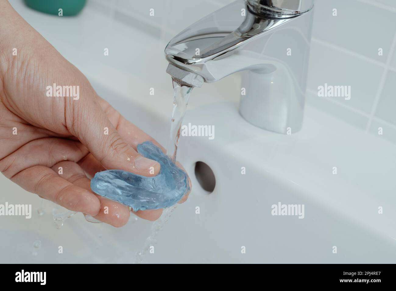 un uomo risciacqua la sua stecca occlusale blu sotto un flusso di acqua di rubinetto nel suo lavandino del bagno Foto Stock