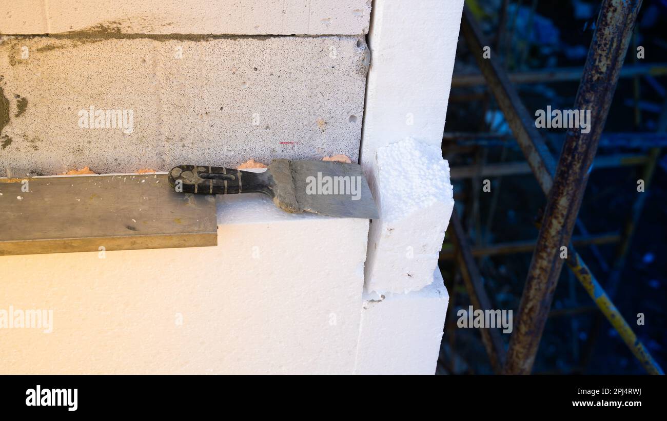 Una vecchia spatola si trova sulla schiuma incollata alla parete della casa. Isolamento di una casa con pareti in mattoni di cemento aerato con polistirolo espanso Foto Stock