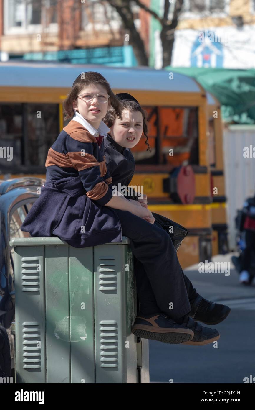 Compagni di classe hasidici seduti in cima a una cassetta di strada Time Warner durante la loro recinta. A Brooklyn, New York. Foto Stock