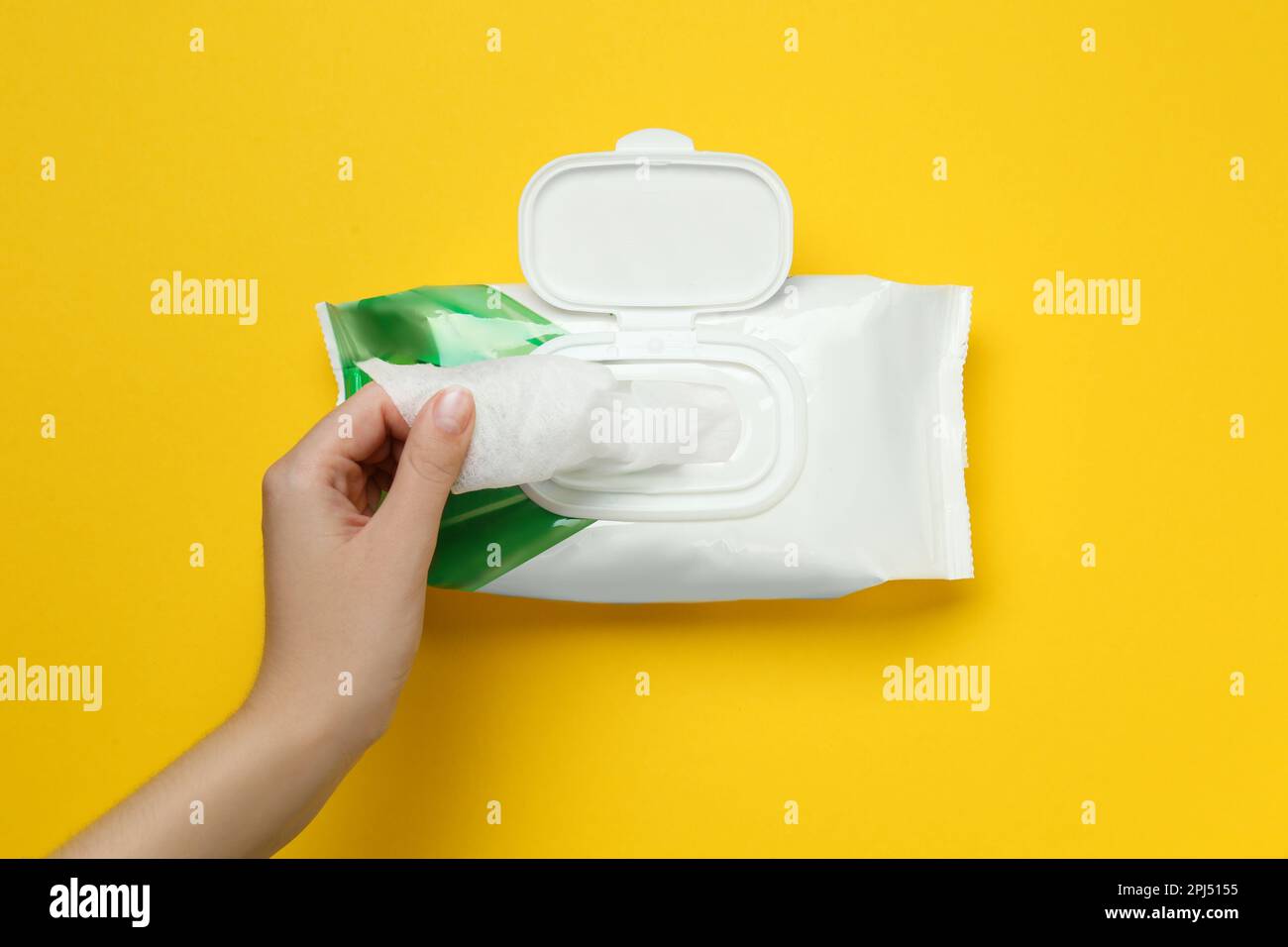 Donna che prende la salvietta bagnata dalla confezione su sfondo giallo, vista dall'alto Foto Stock
