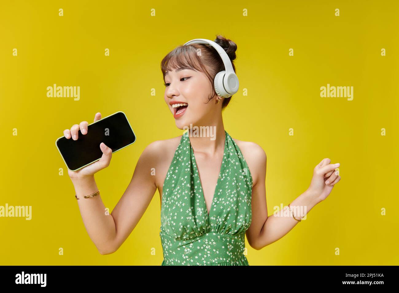 Foto di adorabile donna alla moda in estate indossare l'ascolto di musica tramite cuffie wireless e tenendo il telefono cellulare Foto Stock