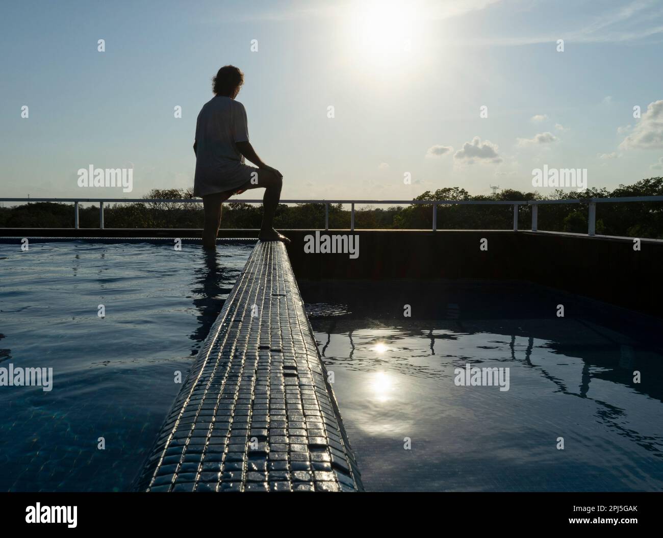 Un uomo solitario, sdraiato in una piscina sul tetto, si rilassa osservando la natura circostante in Messico. Foto Stock