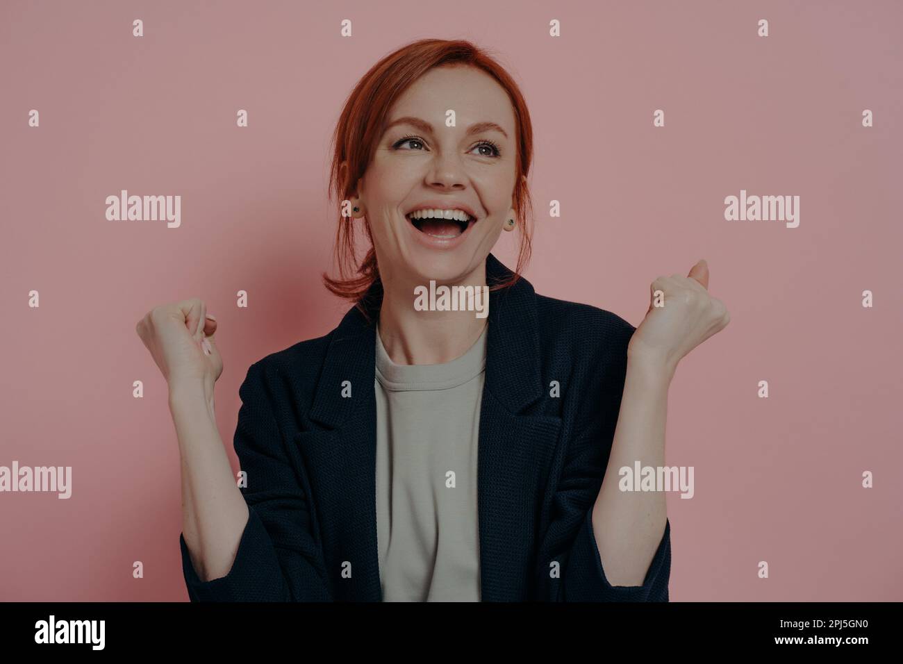 Ritratto di felice eccitata rossa femmina con pugni in rilievo che celebra la vittoria o piange e urla con eccitazione e felicità, isolato su rosa Foto Stock