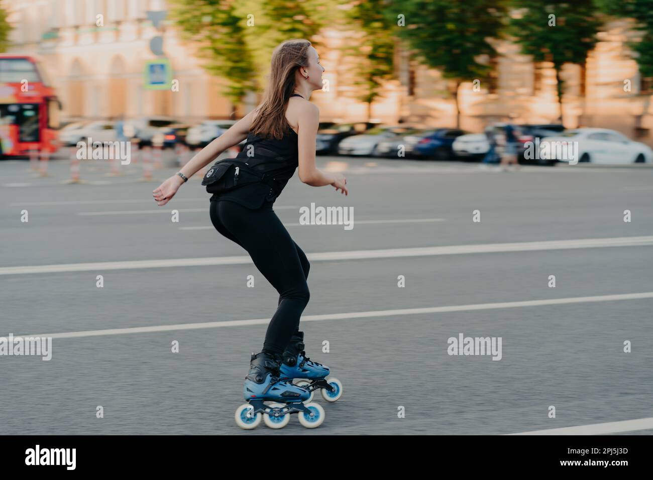 Stile di vita attivo e concetto di hobby. Sportivo giovane donna fa sport all'aperto passeggiate rollerblading vestito in sportsclothes gode di attività di fitness posa Foto Stock