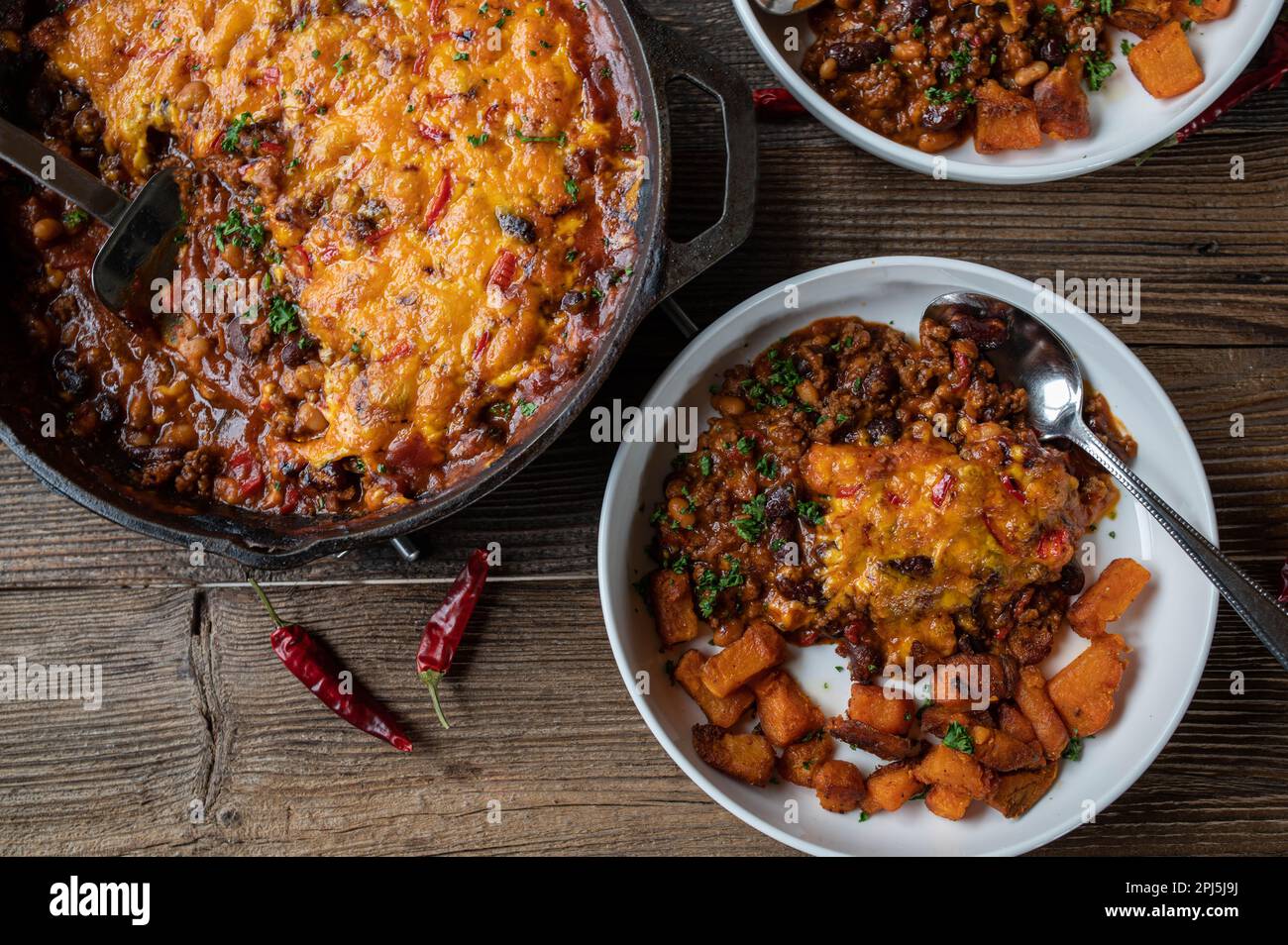 Stufato di fagiolo con formaggio cheddar, condimento al peperoncino e patate dolci arrostite sul tavolo di legno dall'alto Foto Stock