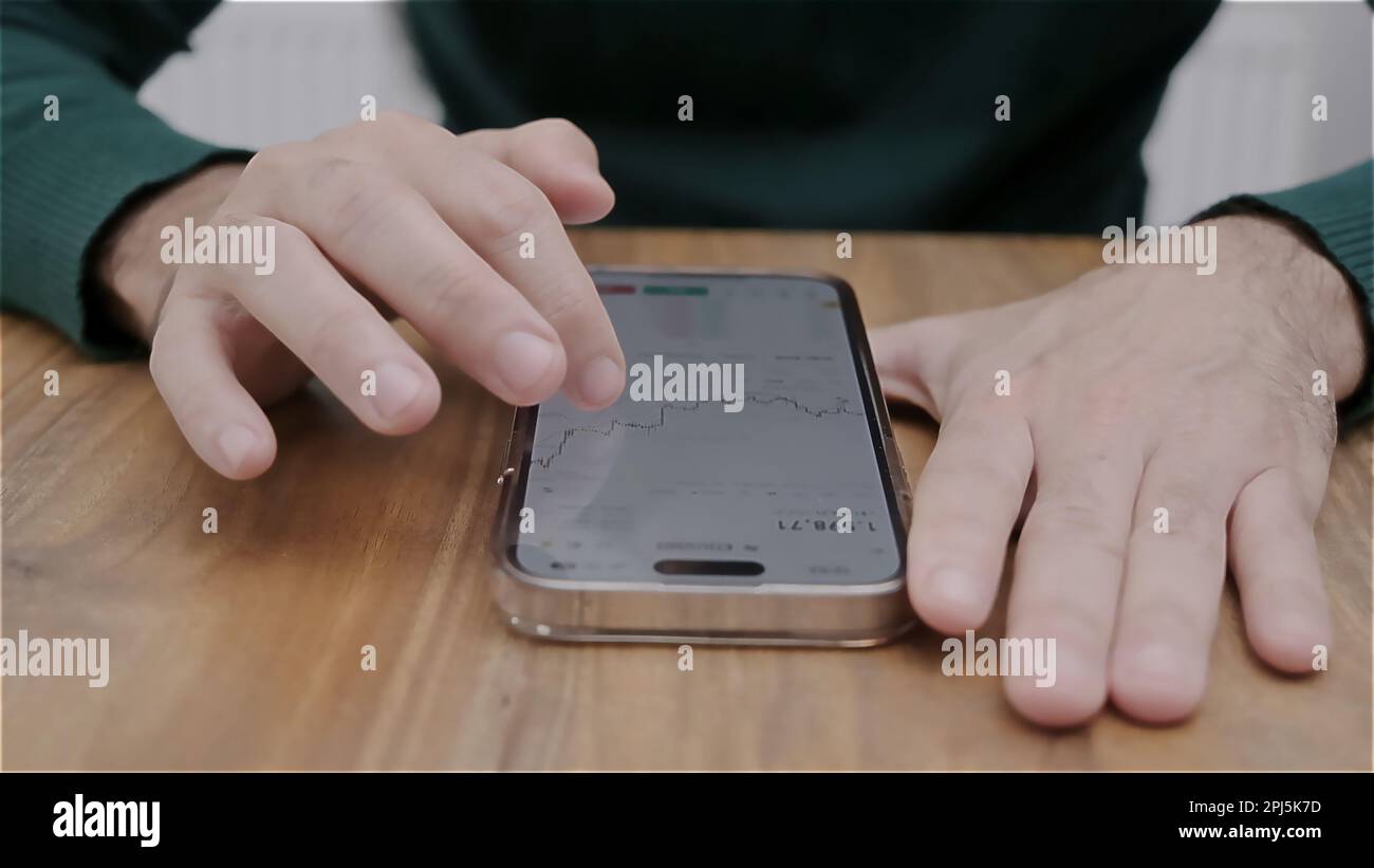Smartphone man hand holding con app per il trading di titoli in valuta sullo schermo. Azioni di analisi finanziaria. Foto Stock