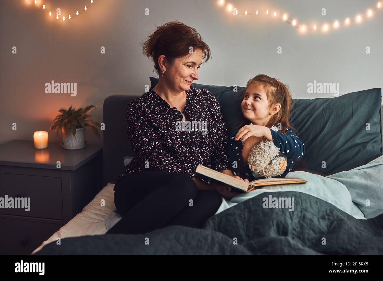 Mamma che legge libro sua figlia a letto prima di andare a dormire. Leggere storie prima di dormire. Storie di sonno per i bambini Foto Stock