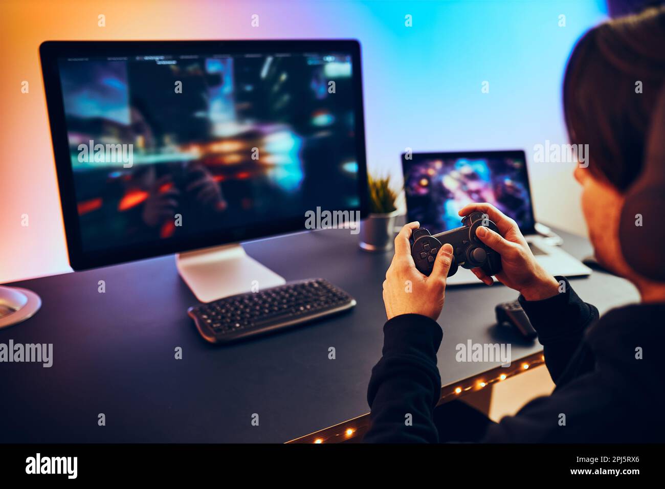 Uomo che gioca a videogame a casa. Gamer che tiene i gamepad seduti davanti allo schermo. Streamer giocare online in una stanza buia illuminata da luci al neon. Competitio Foto Stock