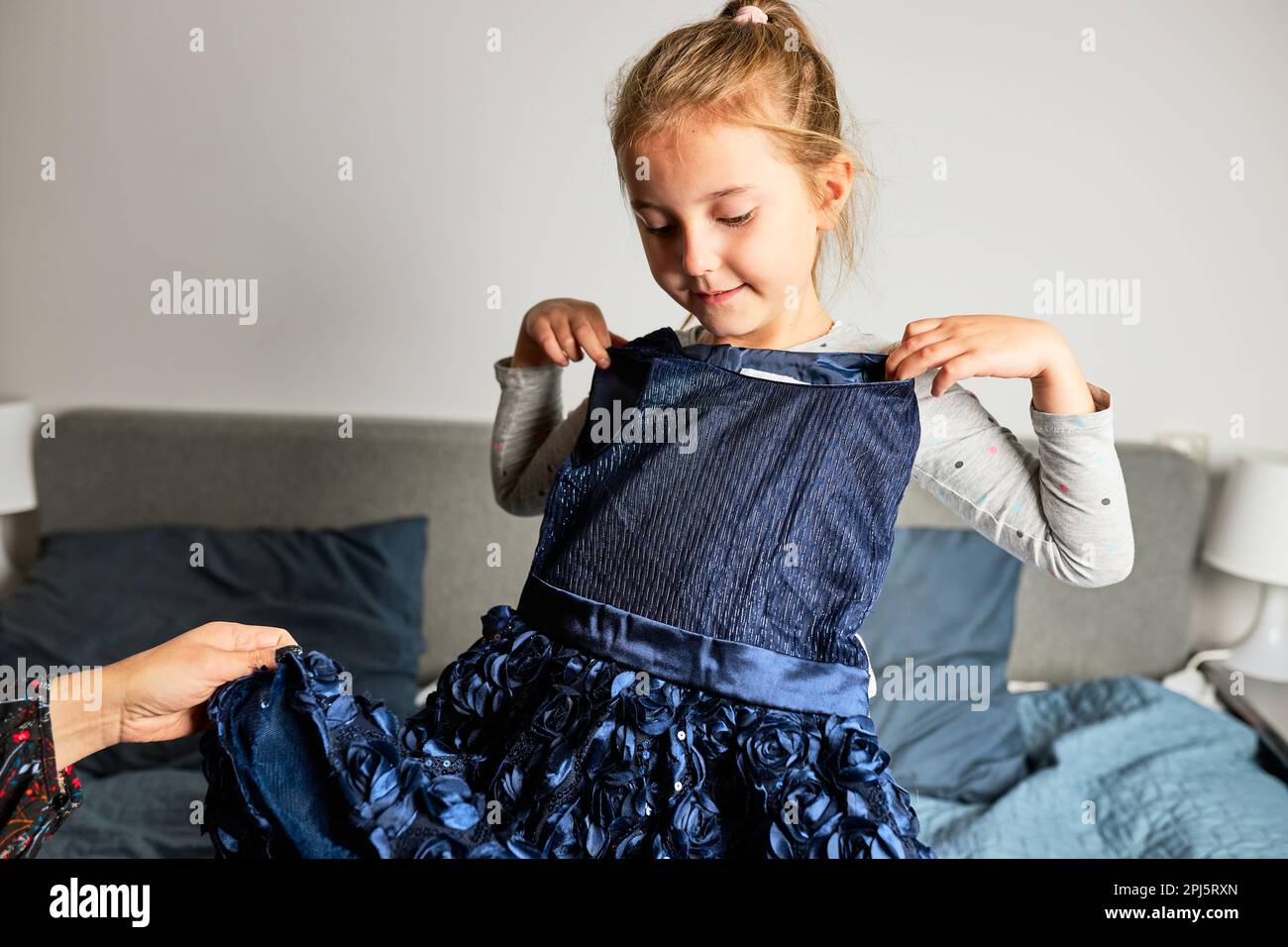 La madre e la sua figlia aprire la scatola con abito ordinato a casa sul divano. Cliente cliente in linea del cliente della mom che tiene l'abito. Servizio di consegna concetto di moda Foto Stock