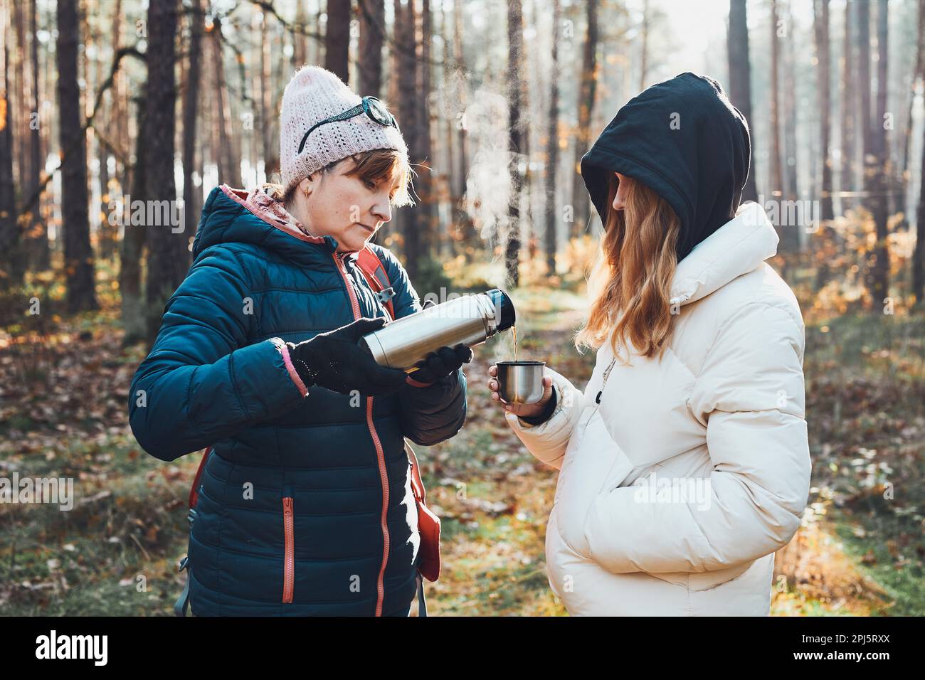 Madre e figlia con zaino in pausa durante il viaggio autunnale versando una bevanda calda da thermos beuta il giorno freddo autunnale. Donne attive che vagano dentro Foto Stock