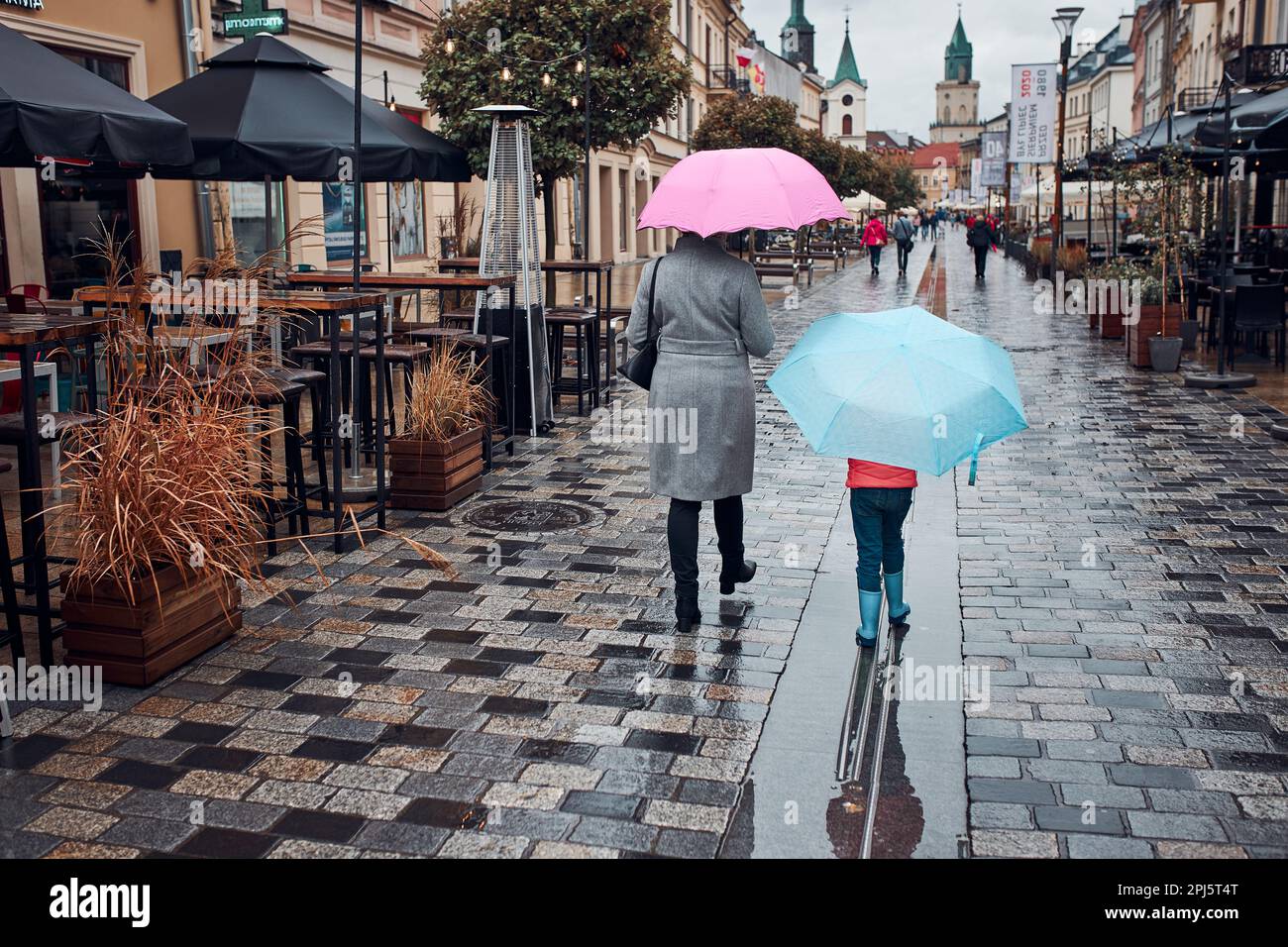 Vista posteriore di madre e sua figlia che tiene gli ombrelloni rosa e blu che camminano in un centro in pioggia giorno d'autunno cupo Foto Stock