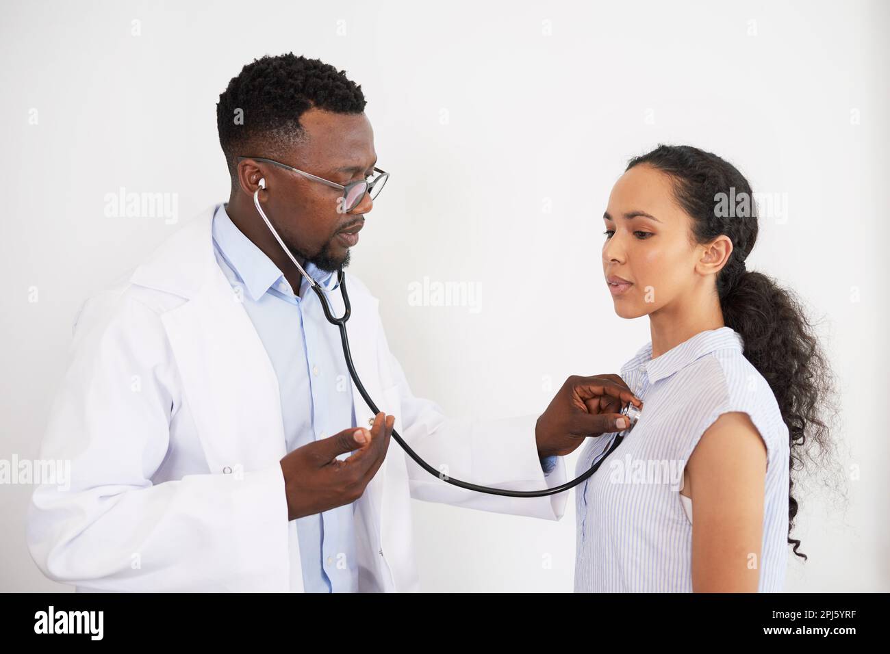Il medico maschio nero ascolta il battito cardiaco della paziente, le dice di respirare Foto Stock