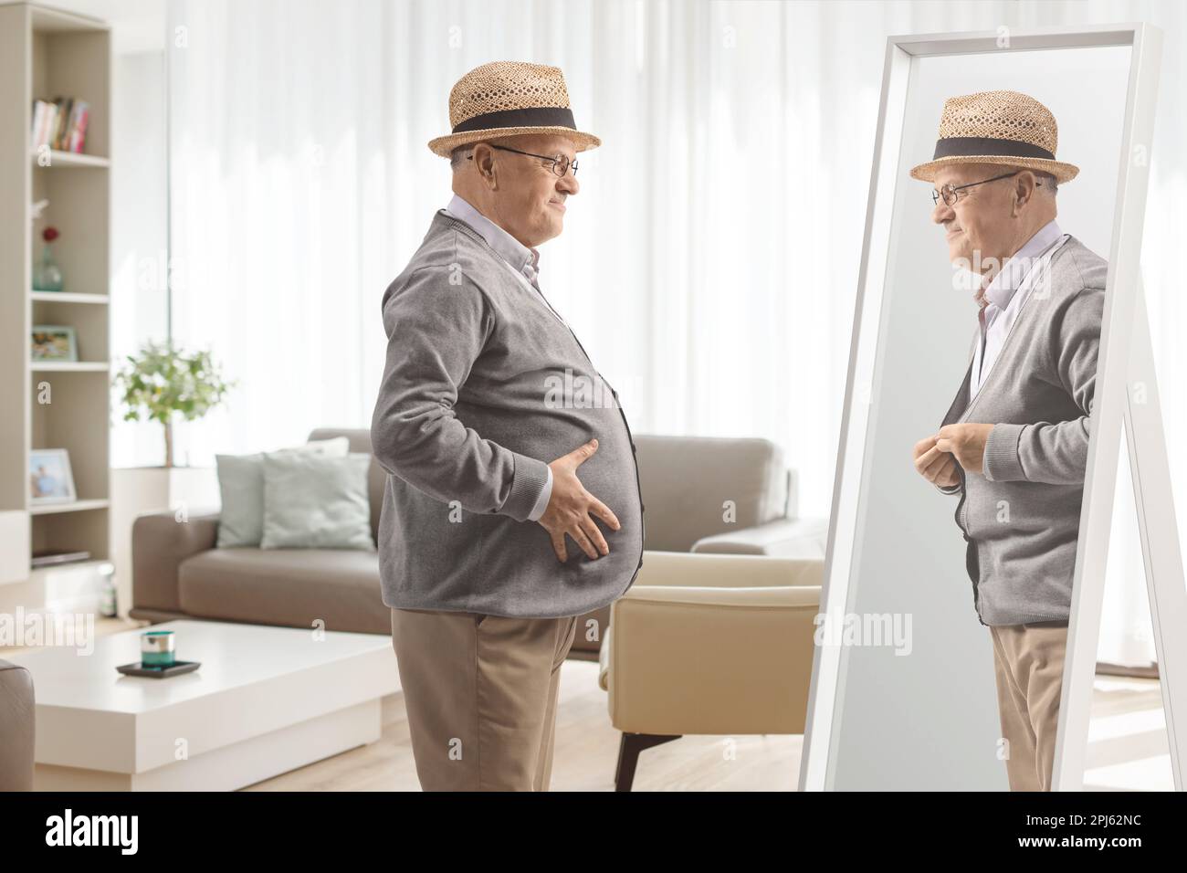 Uomo anziano con una grande pancia che guarda uno specchio e immagina di sé con un corpo sottile a casa Foto Stock