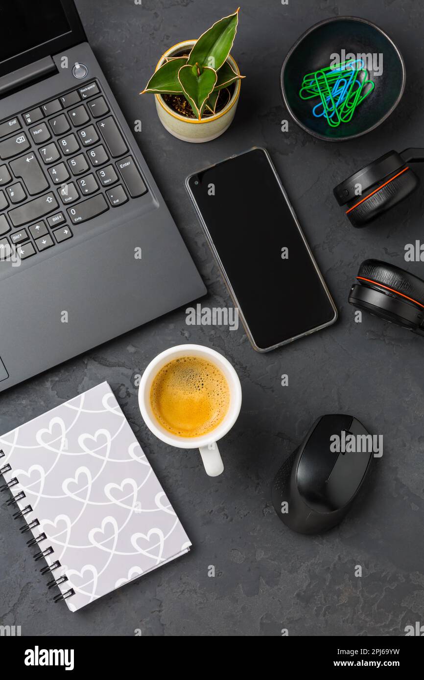 Area di lavoro e scrivania con caffè, computer portatile, cuffie e smarthpone. Piatto in tonalità nera Foto Stock