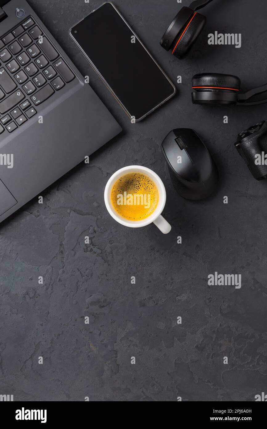 Area di lavoro e scrivania con caffè, computer portatile, cuffie e smarthpone. Piatto in tonalità nera Foto Stock