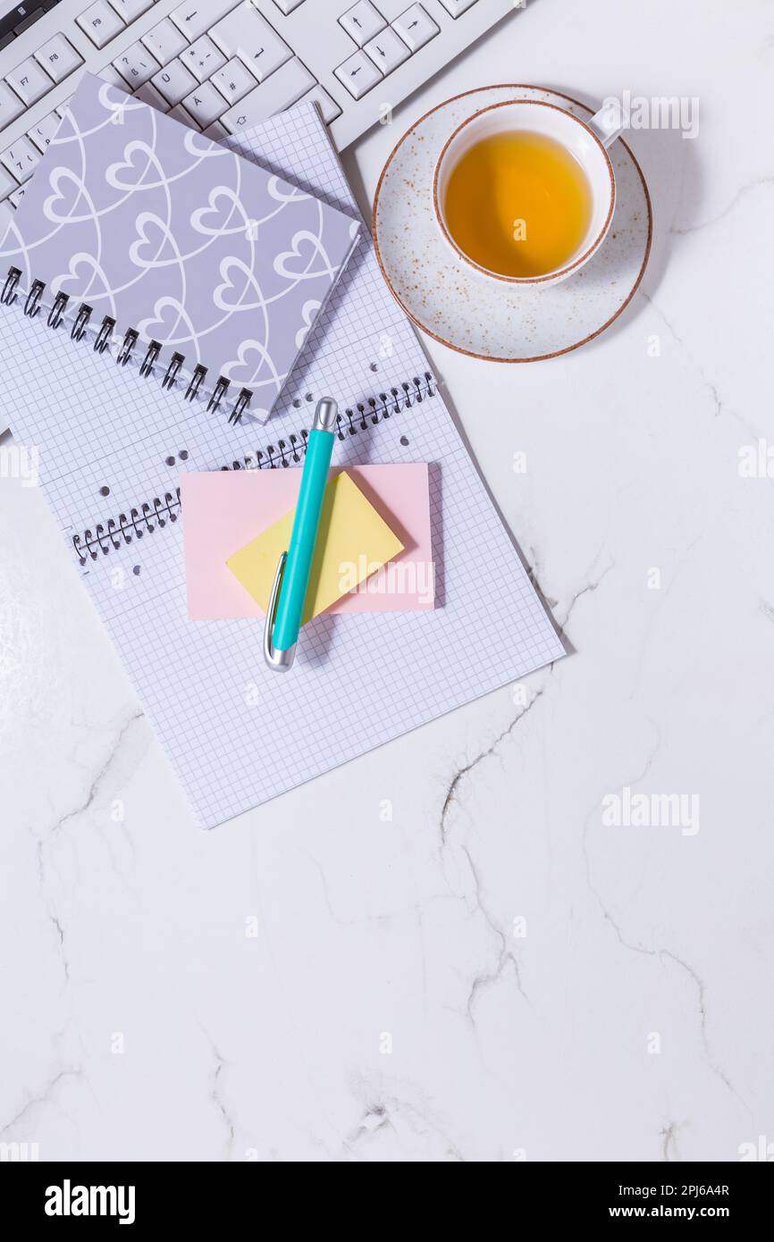 Scrivania da lavoro a casa piatta - tazza di tè, con dispositivo di comunicazione e strumenti di scrittura. Femminile business mockup, copyspace, sfondo bianco Foto Stock